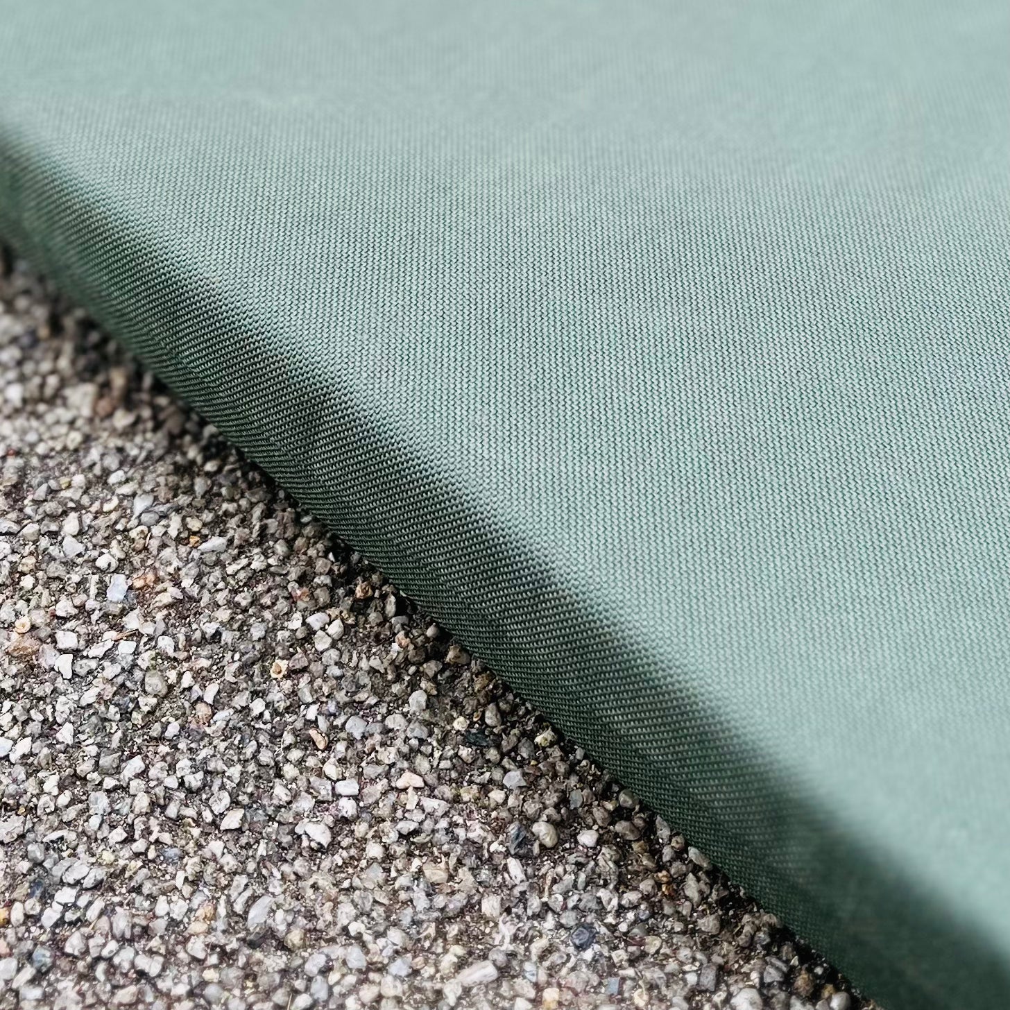 Nahaufnahme des Esschert | Kniekissen von Eschert Design - das grüne, strukturierte Gartenkissen ruht auf einem rauen, gesprenkelten grauen Untergrund, dessen Kante diagonal über das Bild verläuft. Perfekt für die Gartenarbeit.