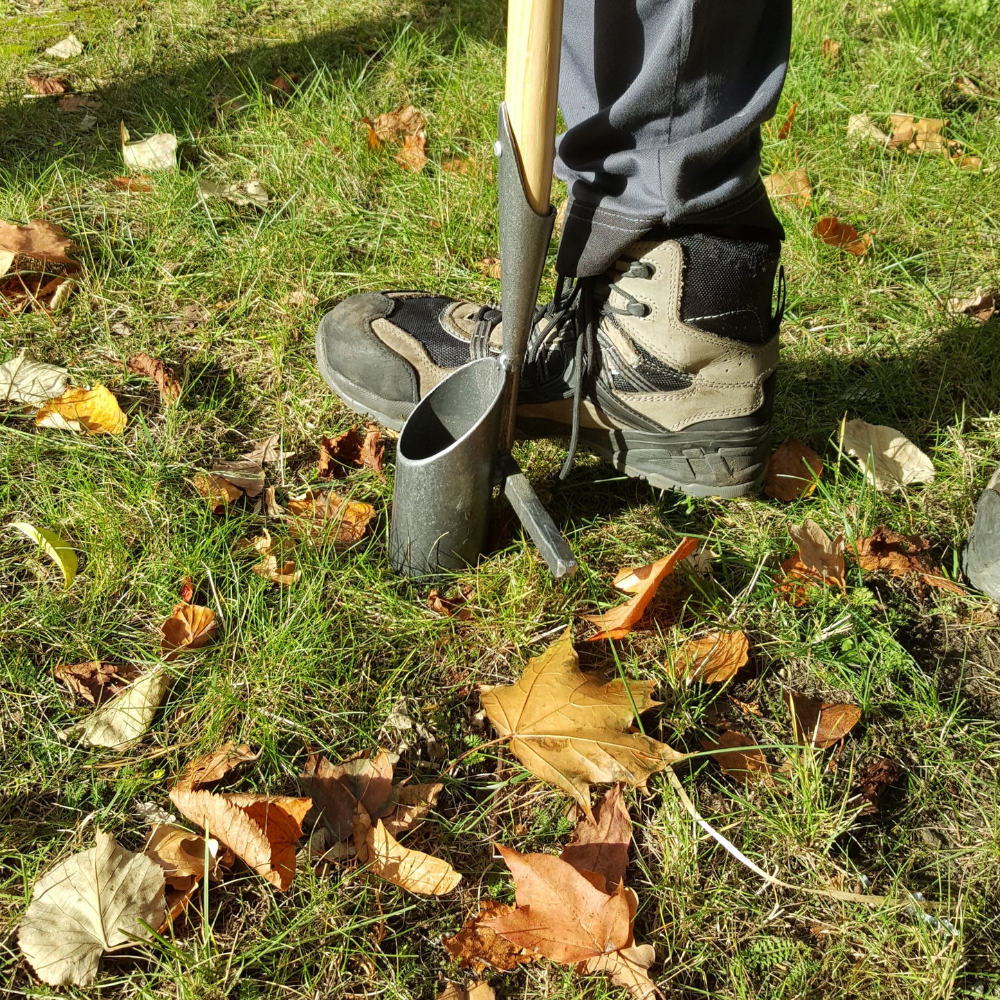 In Wanderschuhen gräbt man mit dem Krumpholz | Zwiebelpflanzer 1349 und einem eschenholz T-Stiel in grasbewachsenen, laubbedeckten Boden und schafft so den idealen Platz für Blumenzwiebeln.